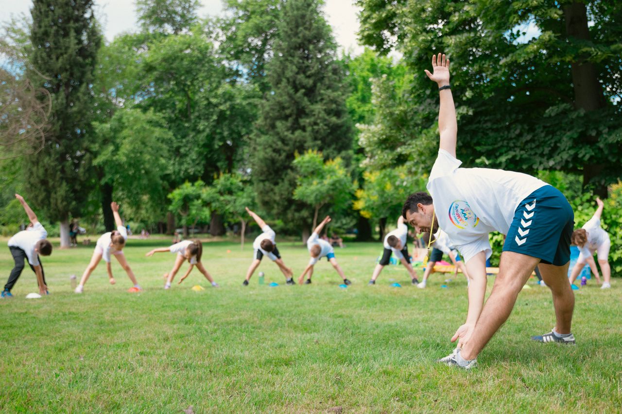 Kids stretching exercises in a park guided by a coach, promoting fitness and fun.