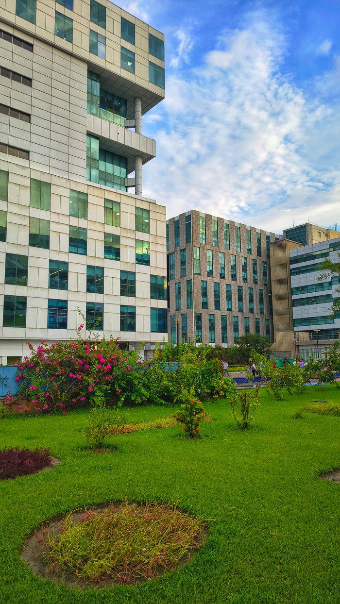 Vertical view of modern office buildings surrounded by lush gardens under a blue sky.